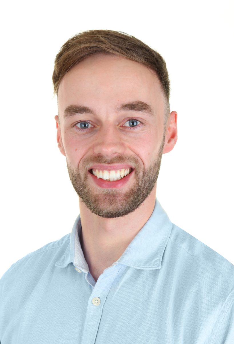 Smiling Joe from DIS Consulting IT wearing a light blue button-up shirt, standing against a plain white background.