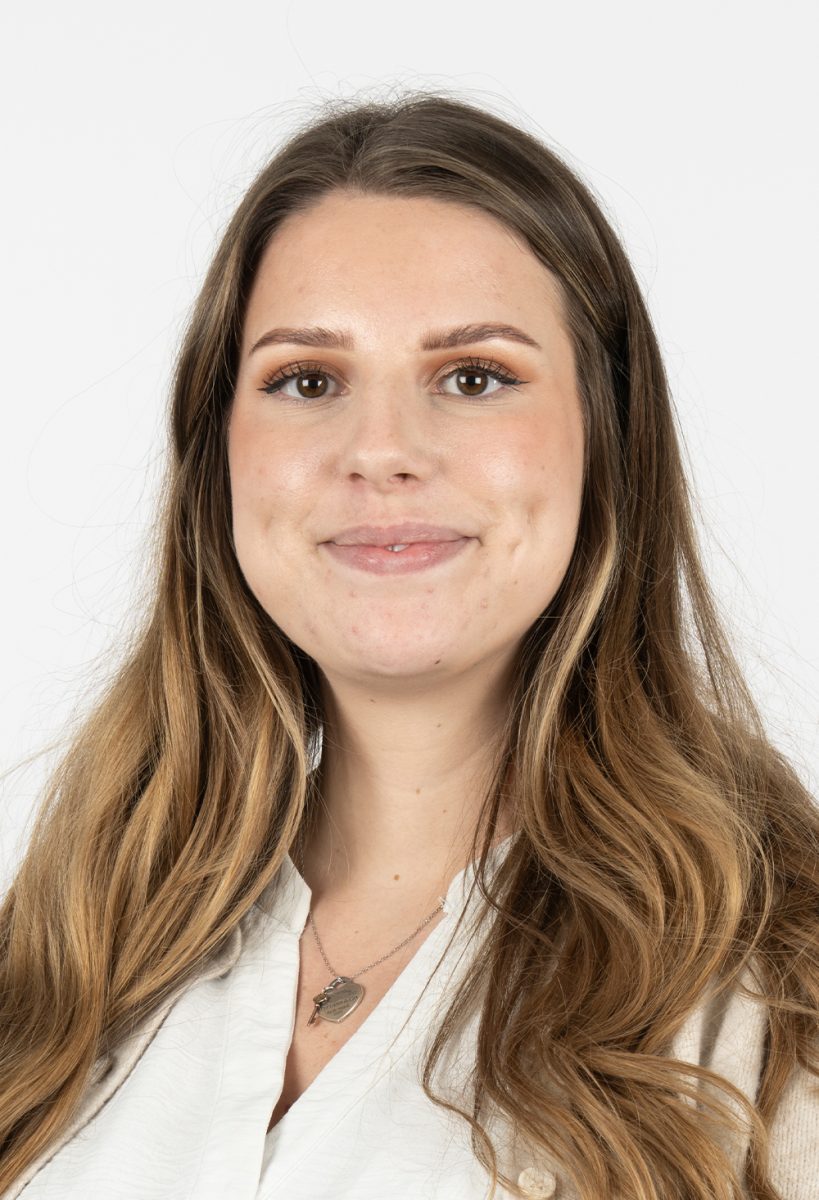 Lilly Farmer from DIS Consulting IT smiling, wearing a cream cardigan and white blouse, standing against a plain light background.