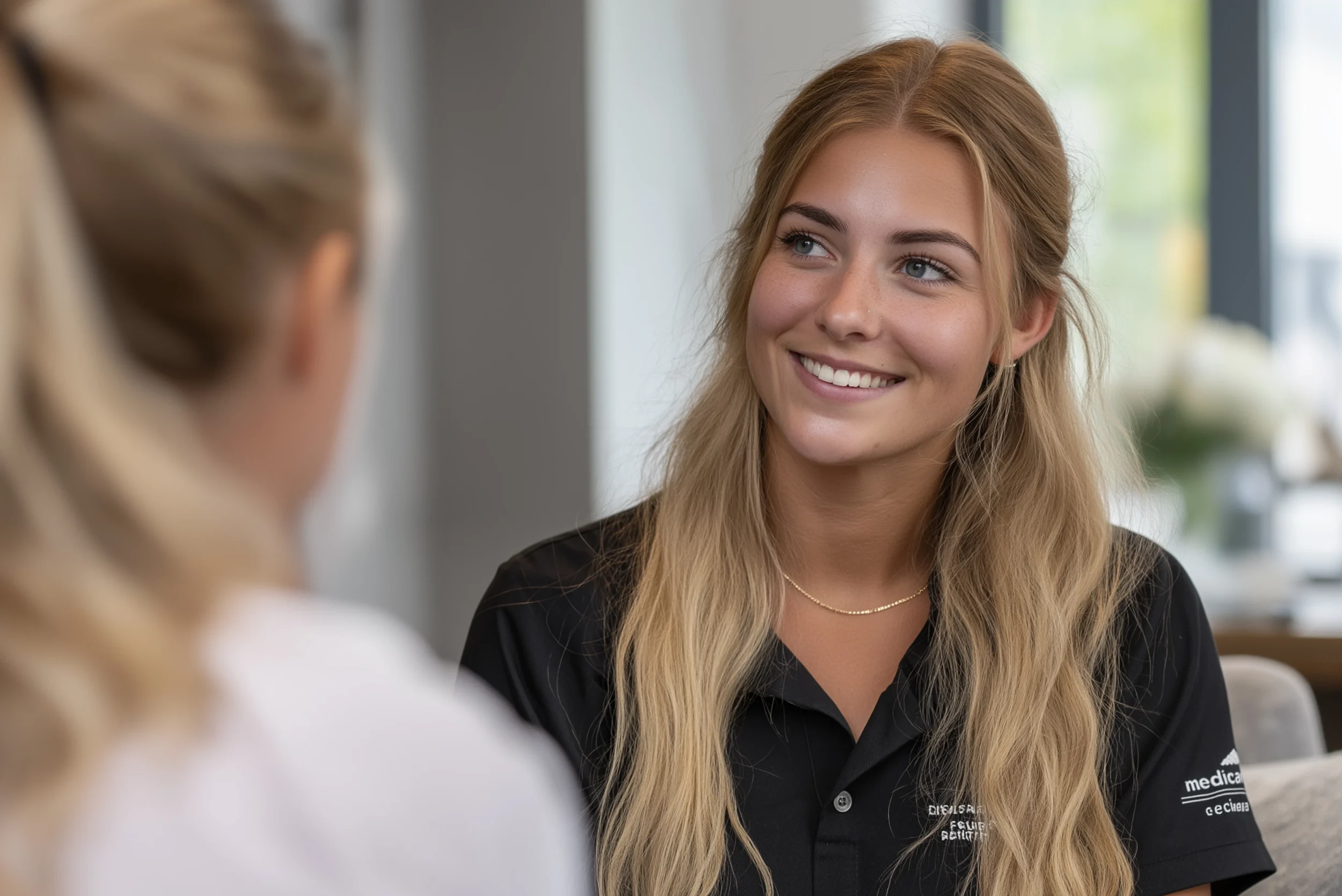 Dental practitioner smiling while speaking with a patient inside a bright, modern clinic.