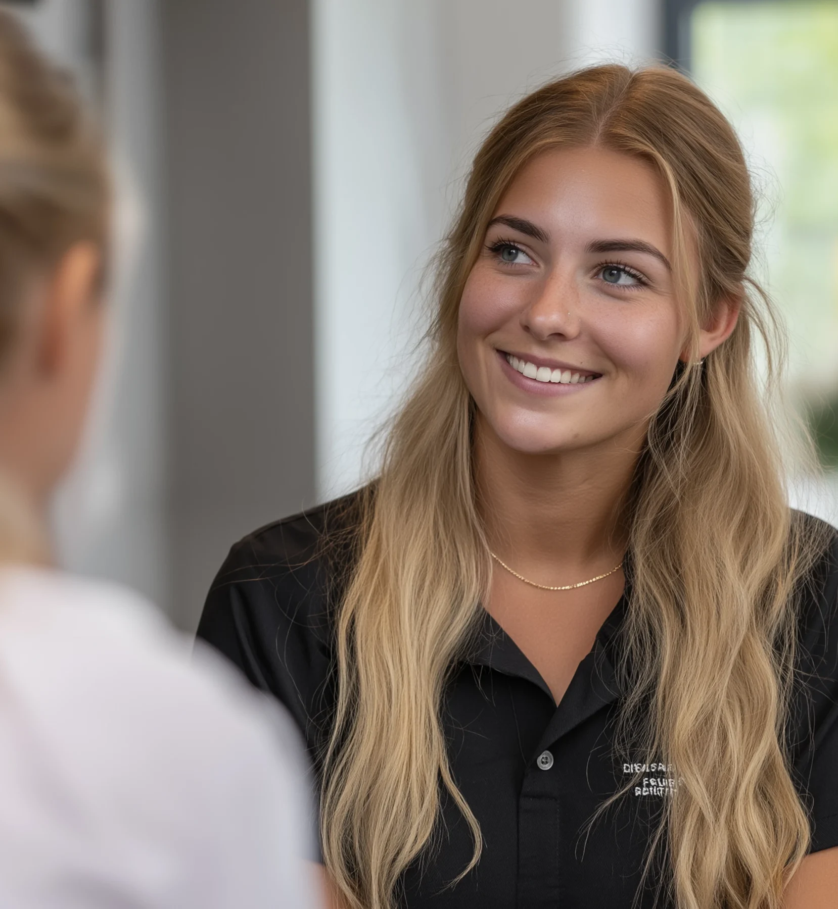 Dental practitioner smiling while speaking with a patient inside a bright, modern clinic.