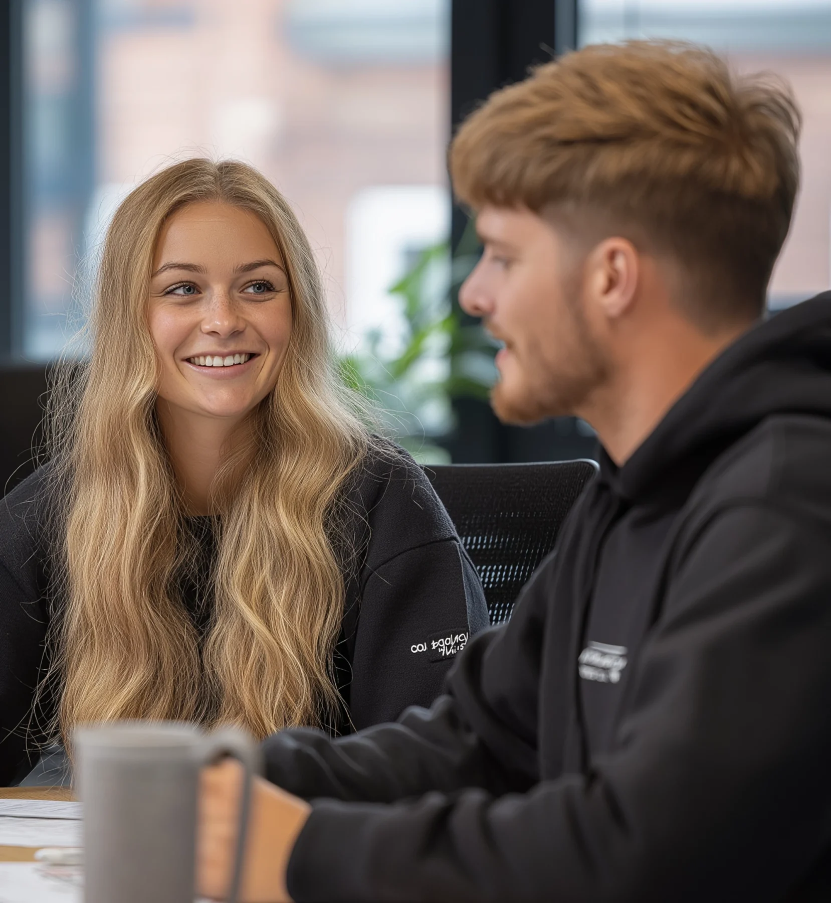 Two young creative professionals chatting and smiling in a modern office environment.