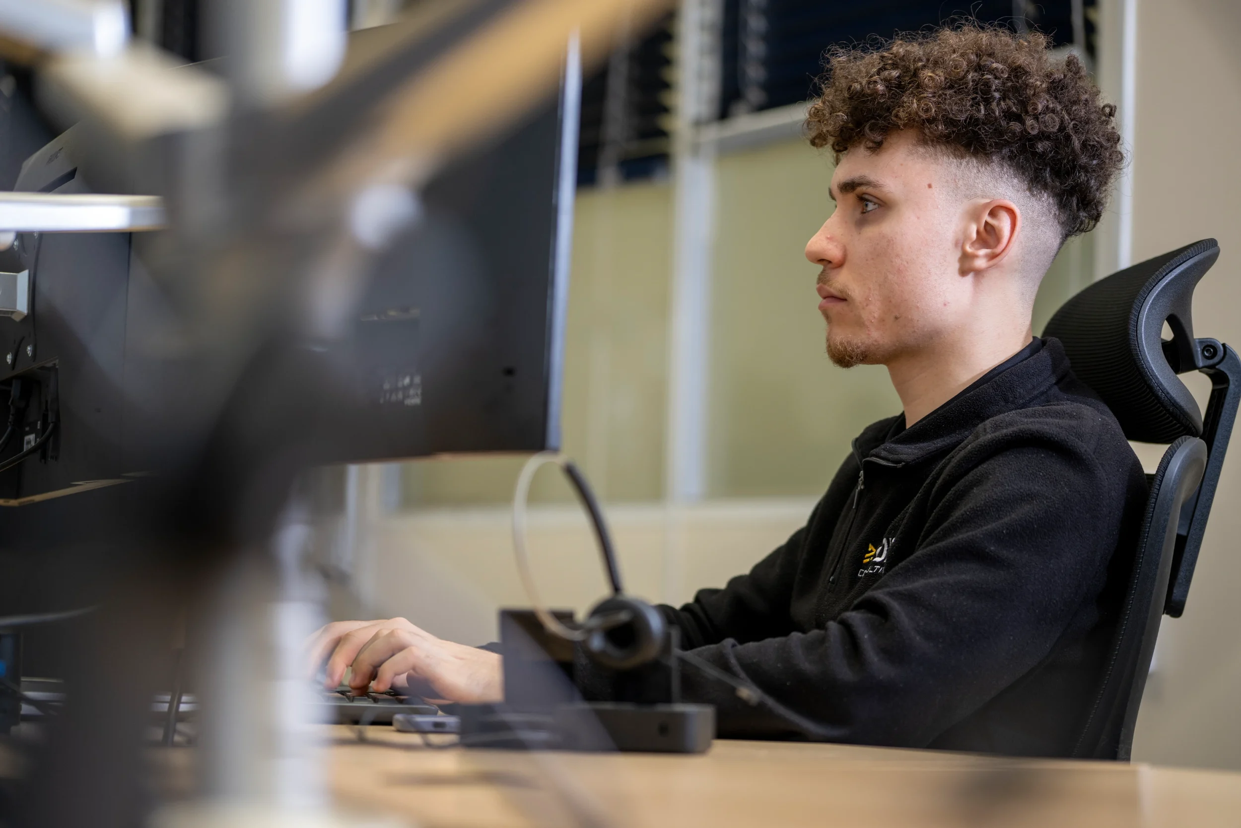 Ethan, a DISConsulting IT support engineer, working at his desk and focusing on a task while typing at a dual-monitor setup.