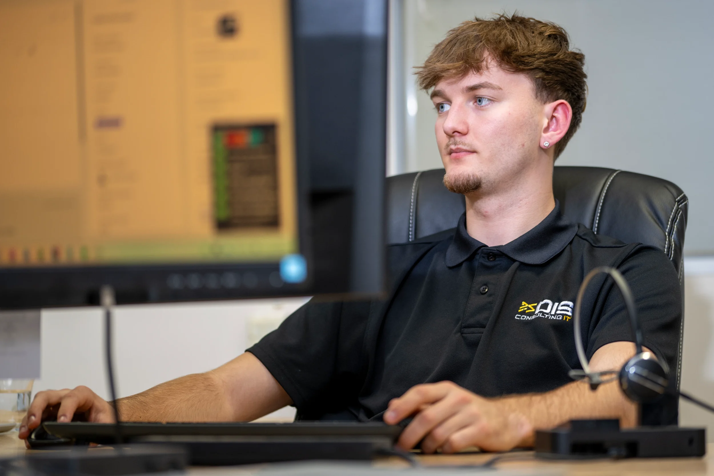 Scott working at his desk in the DISConsulting IT support office, focused on resolving a task across dual monitors.